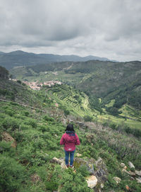 Rear view of woman standing on mountain against cloudy sky