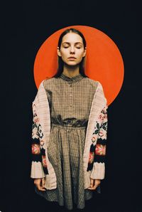 Young woman with eyes closed standing against orange shape and black background