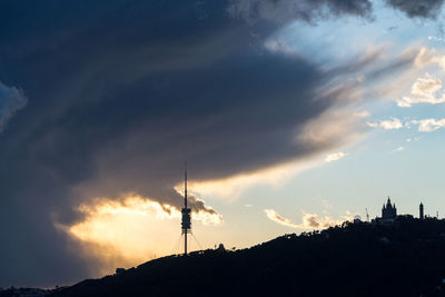 Silhouette communications tower and building against sky during sunset