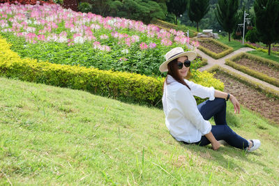 Portrait of beautiful woman sitting on grassy field against plants at park