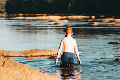 Rear view of shirtless boy in lake
