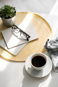 Office desk with coffee cup, succulent plant, eyeglasses and notepad.