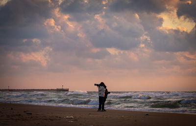 Rear view of woman standing at beach against sky during sunset