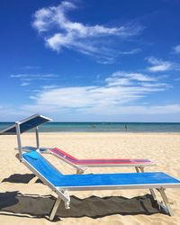 Deck chairs on beach against blue sky