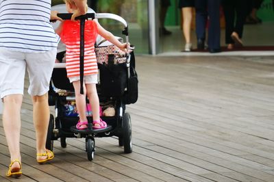 Low section of woman pushing daughter on cart