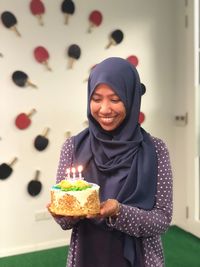 Smiling woman wearing hijab while holding illuminated birthday cake