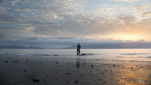 Woman with dog on beach during sunset