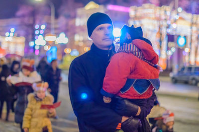 Father carrying child on street in illuminated city at night