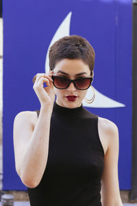 Young woman wearing sunglasses standing against blue wall
