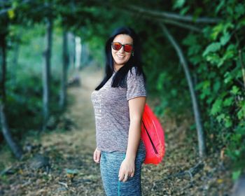 Portrait of smiling young woman wearing sunglasses standing against trees