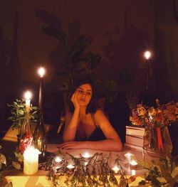 Portrait of woman sitting at illuminated christmas tree at night