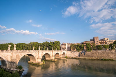 Arch bridge over river by buildings against sky