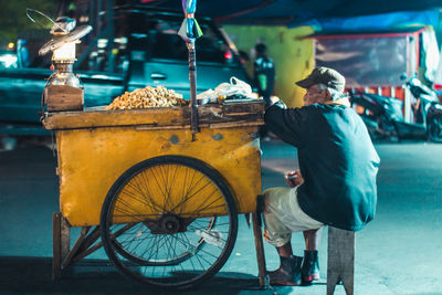 Full length of vendor sitting by cart