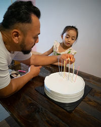 Father igniting birthday candles on cake with daughter