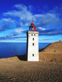 Lighthouse by sea against cloudy blue sky on sunny day