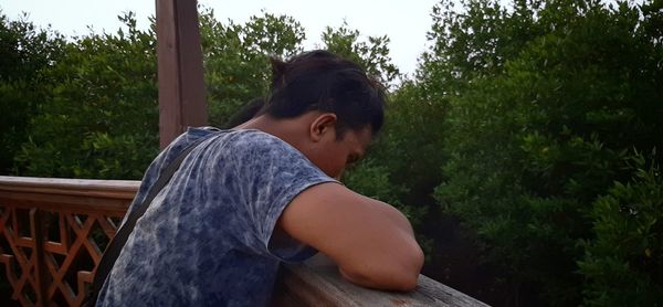 Side view of man standing by railing against trees