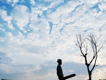 Silhouette man standing by bare tree against sky