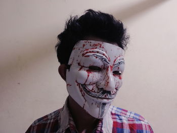 Close-up of young man wearing mask standing against wall during halloween