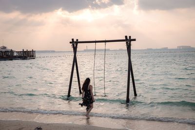 Rear view of woman standing on beach against sky during sunset