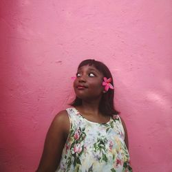 Black woman with short bob cut flowers in her ears, wearing a floral dress. pink wall as background. 