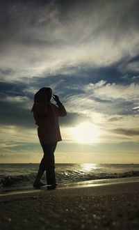 Woman photographing sea against sky during sunset