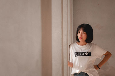 Portrait of a young woman standing against wall