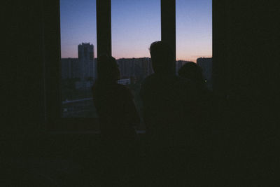 Silhouette people standing in city against sky seen through window