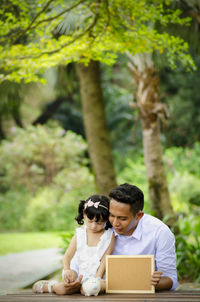 Couple sitting on plant against trees