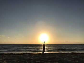 Silhouette man standing on beach against sky during sunset