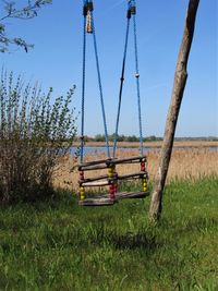 Empty swing hanging on field against clear sky