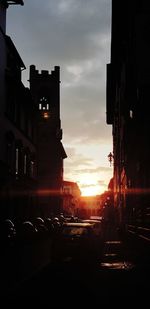 Cars on road amidst buildings against sky during sunset