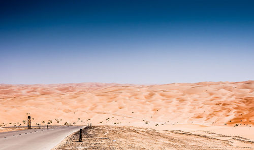 Road leading towards desert against clear sky