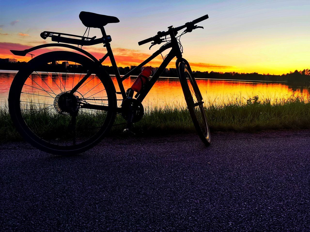BICYCLE PARKED ON ROAD AGAINST SKY DURING SUNSET