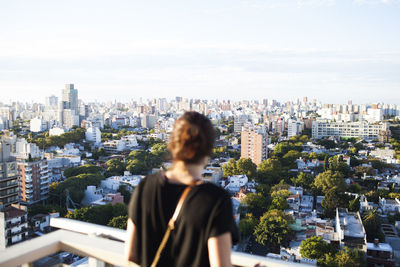 Rear view of woman standing at building terrace against cityscape