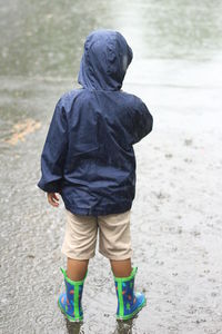 Rear view of boy standing on puddle collected on road during rainy season