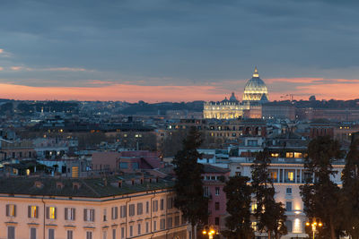 Illuminated buildings in city against cloudy sky at dusk