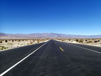 Empty road leading towards mountain against clear sky