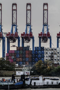 Cranes at harbor against sky in city