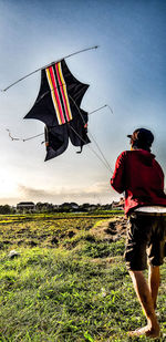 Rear view of men flag on field against sky