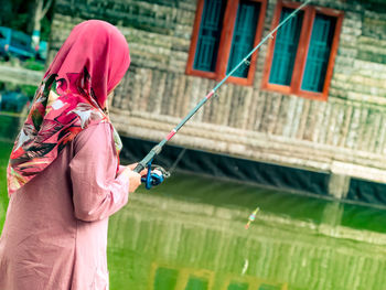 Side view of woman with umbrella standing against built structure