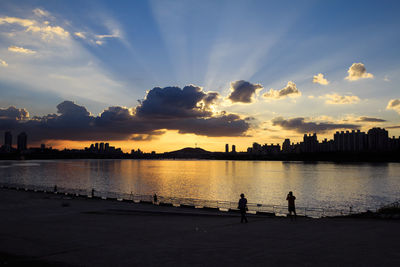 Silhouette people by sea against sky during sunset