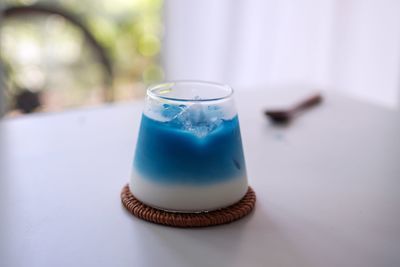 There is a beautiful blue butterfly tofu pudding drink in the transparent glass on the white table