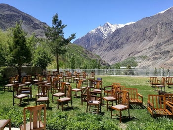 Empty chairs and tables on field by mountains against sky