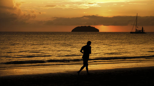 Silhouette man standing on beach against sky during sunset