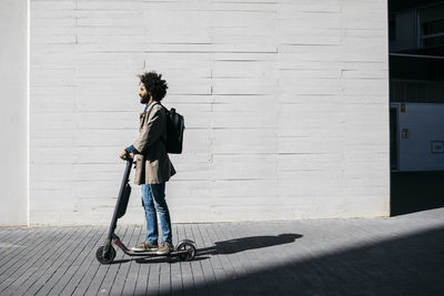 Man with backpack standing on e-scooter