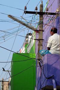 Man sitting by cables against clear sky