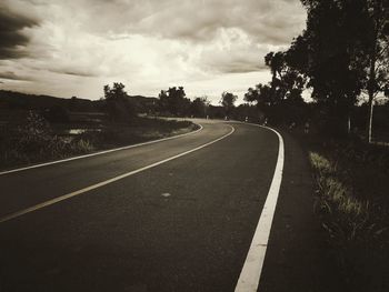 Empty road along trees and against sky