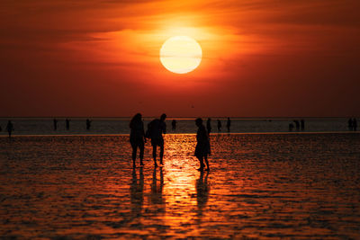 Silhouette people on beach against sky during sunset