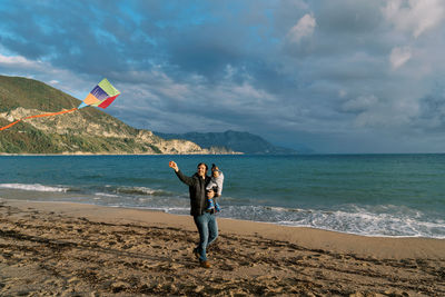 Rear view of woman standing at beach against sky