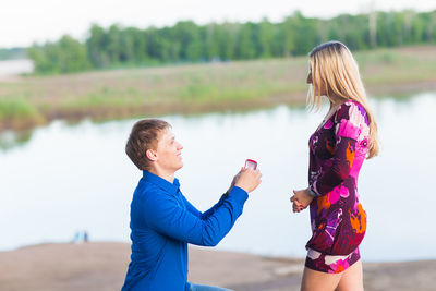 Rear view of friends standing by lake against blurred background